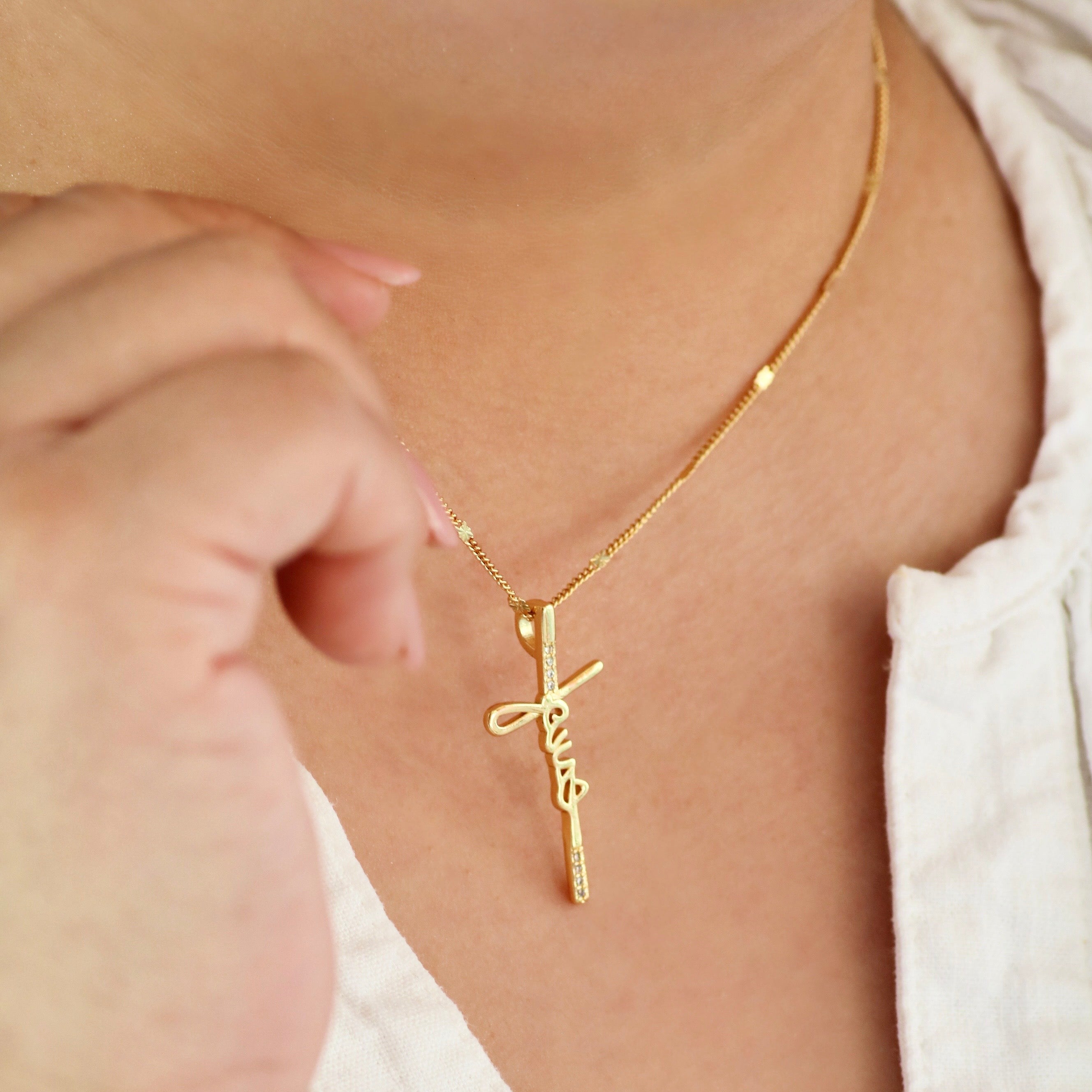 Gold necklace with a cross pendant on a person wearing a white top.