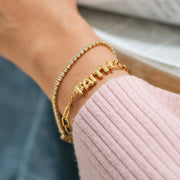 Gold bracelet with 'FAITH' on a wrist against a blurred background