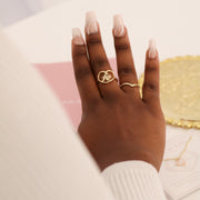 Hand wearing a gold ring with a heart design on a blurred background