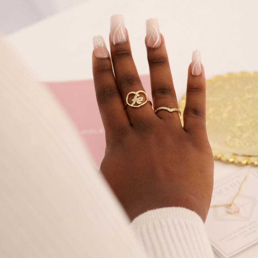 Hand wearing a gold ring with a heart design on a blurred background