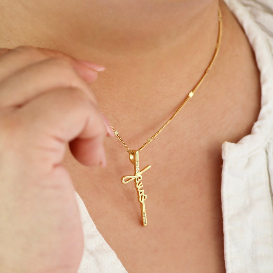 Gold necklace with a cross pendant on a person wearing a white top.