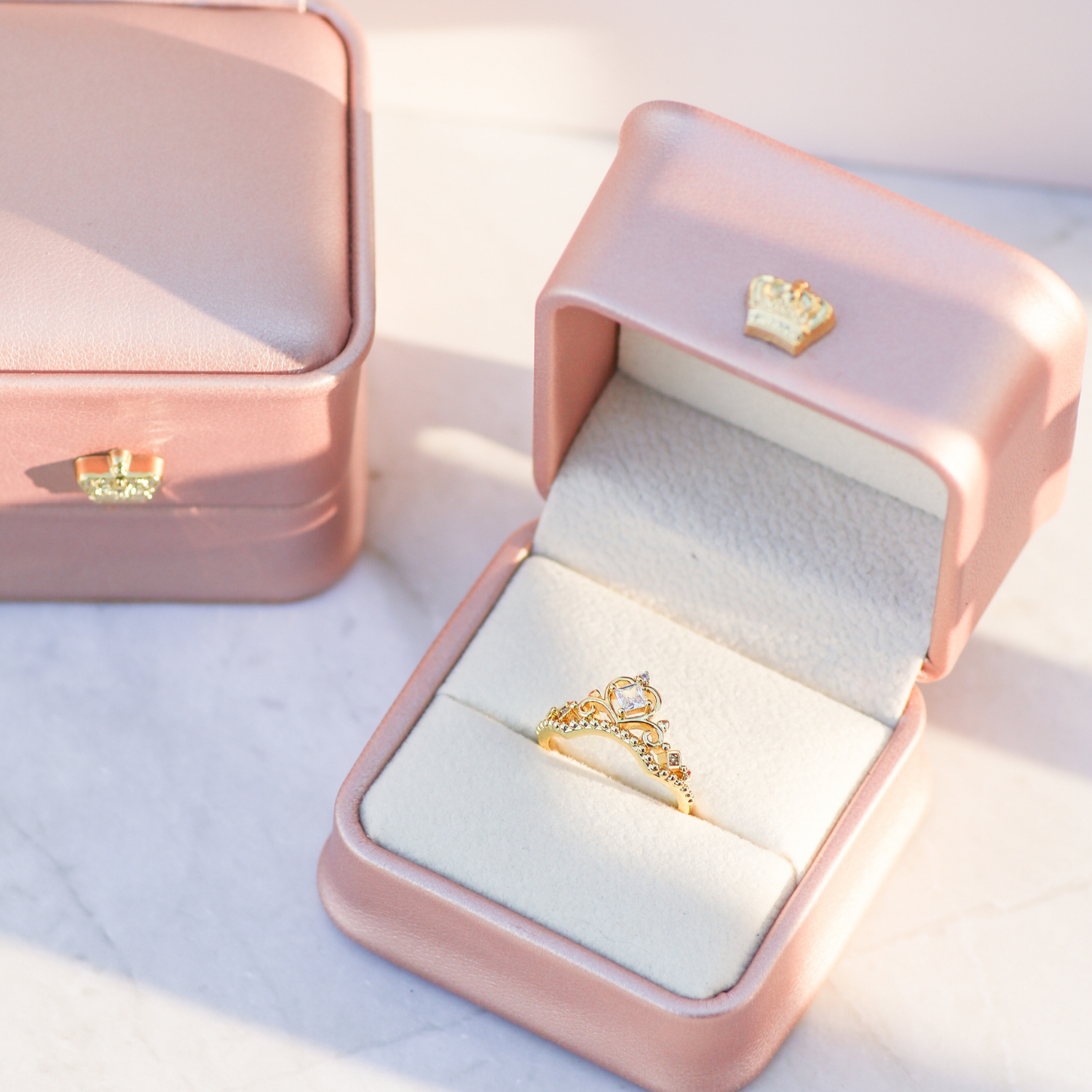 Gold ring with a crown design in an open pink jewelry box on a light background