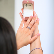Person holding a ring with a pink jewelry box in the background