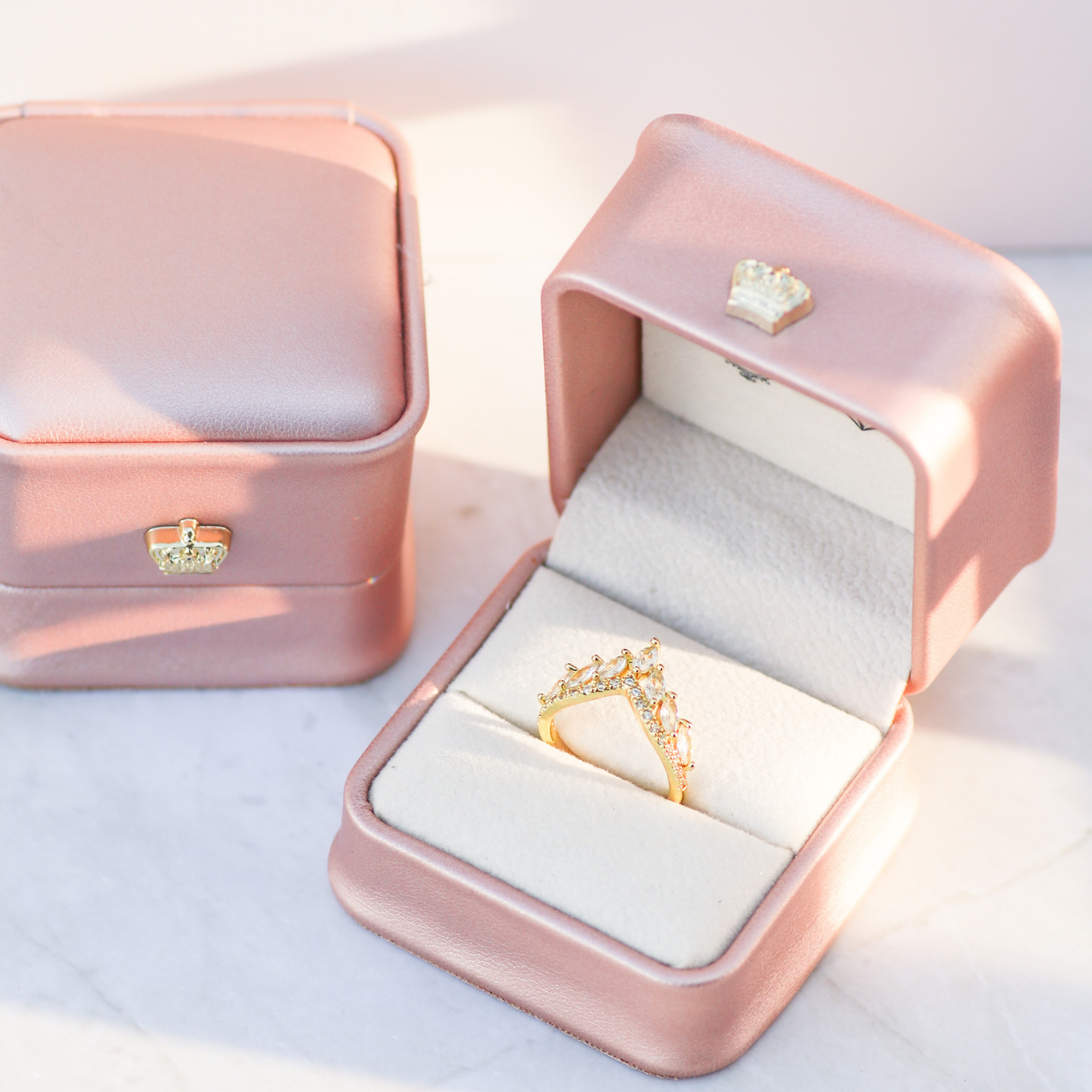 Pink jewelry box with a gold ring inside on a light background